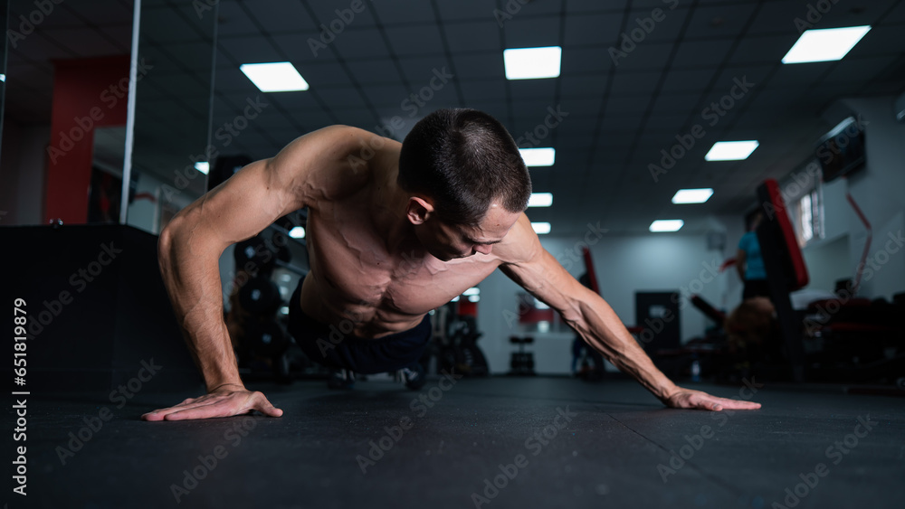 Fototapeta premium Muscular shirtless man doing push ups in the gym. 
