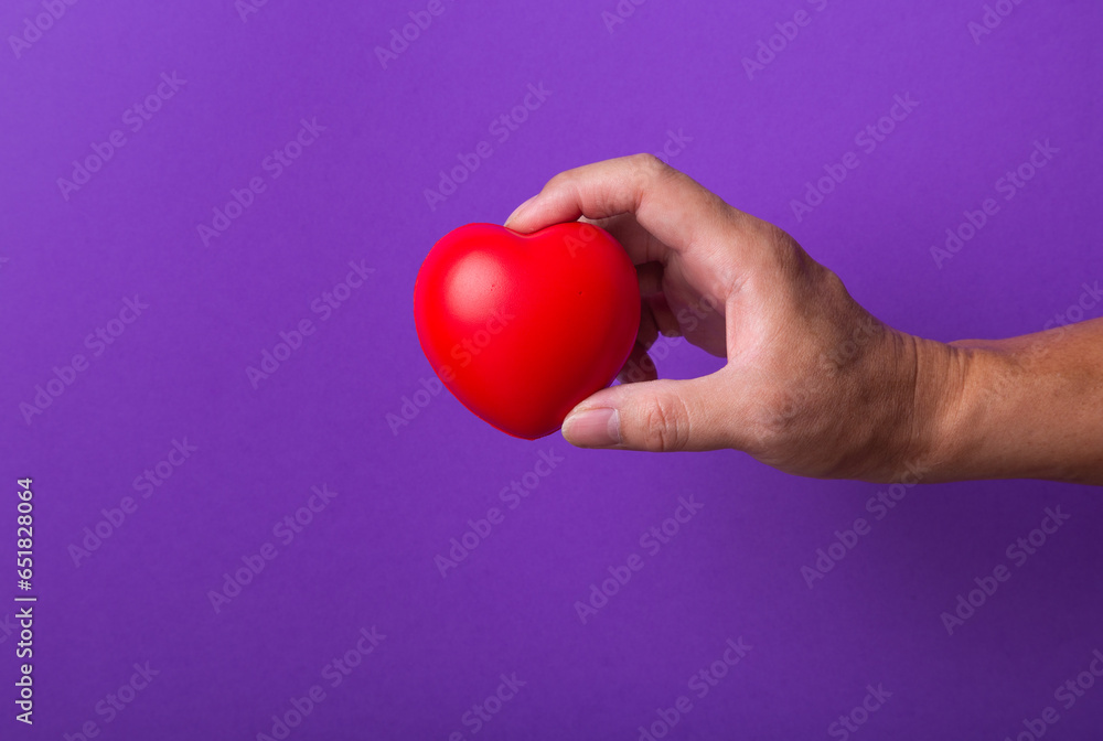 Obraz premium Hand with red heart on purple background.