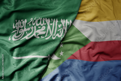 big waving realistic national colorful flag of saudi arabia and national flag of comoros .