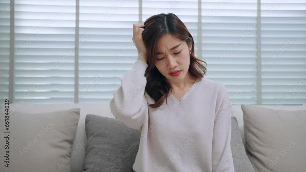 Young beautiful asian woman sitting on sofa massaging head getting sick headache migraine and feeling stress in living room at home. Healthcare and medical concept