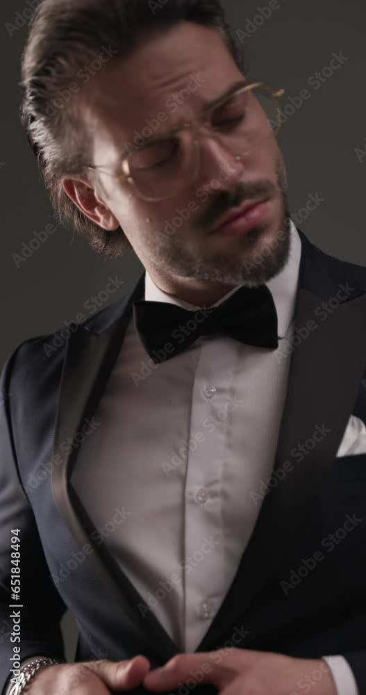 unshaved young man unbuttoning tuxedo, moving and walking away with hands in pockets in front of colorful background unshaved young man unbuttoning tuxedo, moving and walking away with hands in pockets in front of colorful background