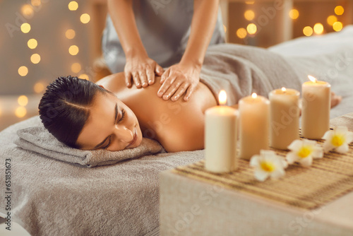 Young woman relaxing in spa salon with hot stones along spine. Beautiful relaxed girl lying on couch enjoying hot stone massage in wellness center. Beauty treatment therapy, body care concept