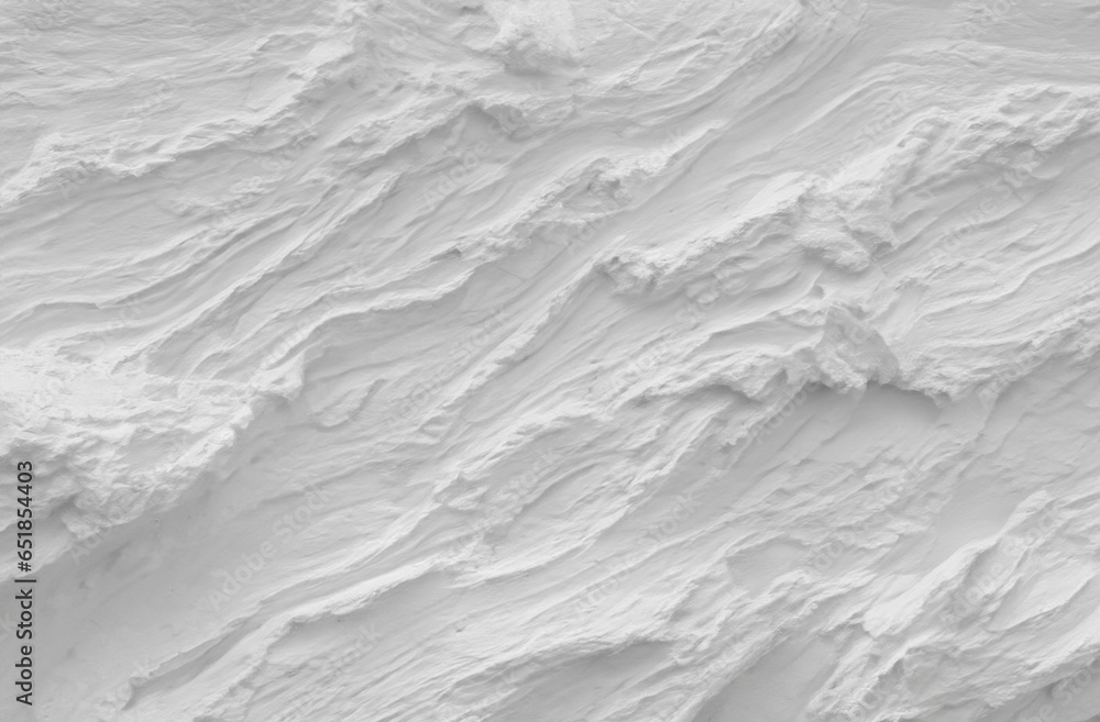 Fototapeta premium A detailed close-up photograph captures the rough, three-dimensional texture of a white plaster or stucco wall surface, featuring an abstract and organic relief pattern created by trowel marks.