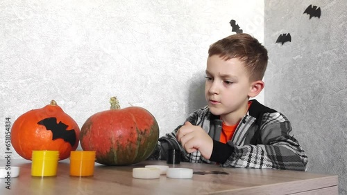 he boy is preparing for Halluin. Preparation of scenery in Halluin. The boy sits at the table and decorates the pumpkin for the holiday photo