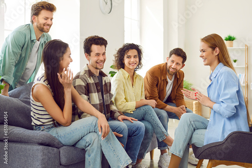 Group of young people hanging out at home. Friends gather at someone's place and have fun together. Happy men and women sitting on couch, talking about college life, sharing stories and telling jokes