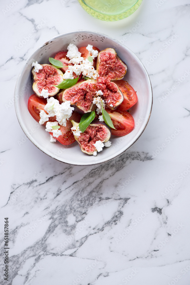 Fig fruits, tomato and goat cheese salad, flat lay on a white marble background, vertical shot with copy space Fig fruits, tomato and goat cheese salad, flat lay on a white marble background, vertical shot with copy space