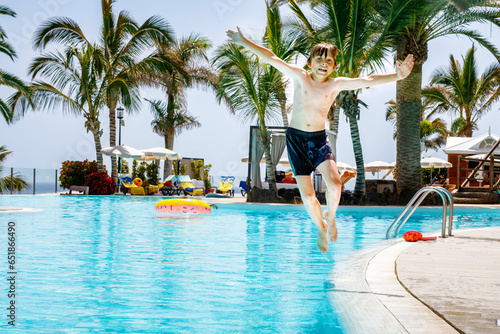 Happy little kid boy jumping in the pool and having fun on family vacations in a hotel resort. Healthy child playing in water. © Irina Schmidt