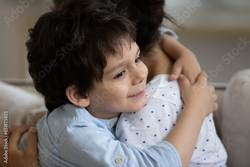 Close up 5s boy hugging Indian mother, family enjoying tender moment, smiling adorable son child and caring young mom embracing, good relationship and trust, sitting on couch, motherhood concept