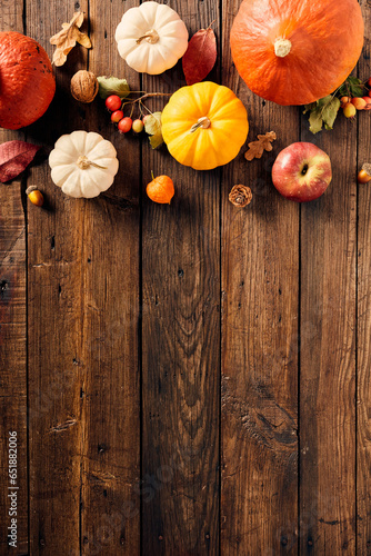 Vertical autumn flat lay composition with pumpkins, fall leaves, red berries, walnuts, pine cones on wooden background. Flat lay, top view, overhead.