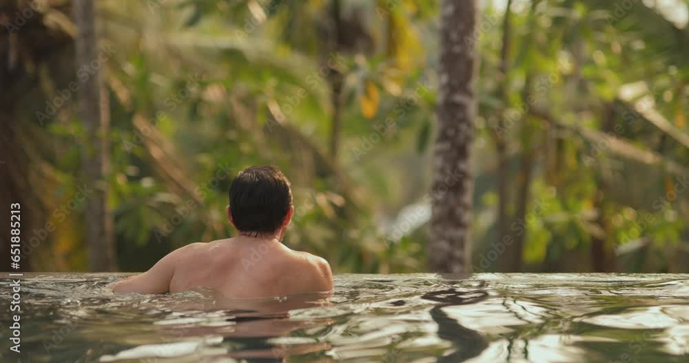 Happy rich vacationer man relaxing and spending time in a tropical open-air swimming pool during summer tropical vacation in a luxury villa. High-quality 4k footage Happy rich vacationer man relaxing and spending time in a tropical open-air swimming pool during summer tropical vacation in a luxury villa. High-quality 4k footage