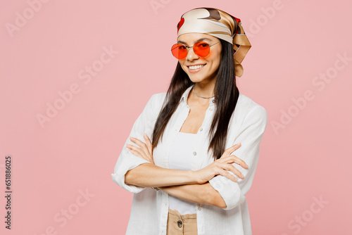 Side view young latin woman she wearing white shirt casual clothes sunglasses hold hnads crossed folded look camera isolated on plain pastel light pink background studio portrait. Lifestyle concept. photo