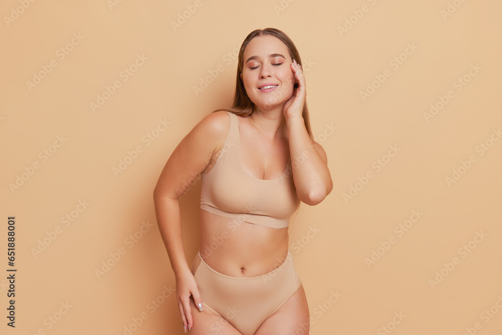 Pretty model dressed in beige underwear posing with closed eyes on background holding one hand on her face, body comfort concept, copy space Pretty model dressed in beige underwear posing with closed eyes on background holding one hand on her face, body comfort concept, copy space