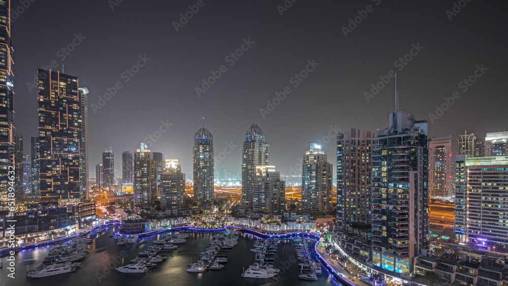 Panorama showing Dubai marina tallest skyscrapers and yachts in harbor aerial night.