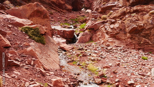 Circulation de l'eau entre des roches rouges ou oranges, dans une zone désertique, sauvage, montagneuse et rocheuse, avec un peu de verdure, jaune et vert, traversée inconnue, eau de source, 