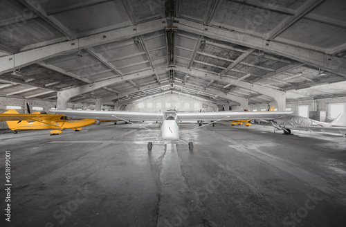 Small airplanes in storage at small aerodrome. Hangar of flying club with light aircraft - propeller driven ones and a glider.  photo