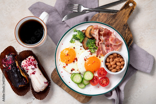 Traditional Englis breakfast plate with bacon strips, sunny side up eggs, vegetables and cake on light background photo