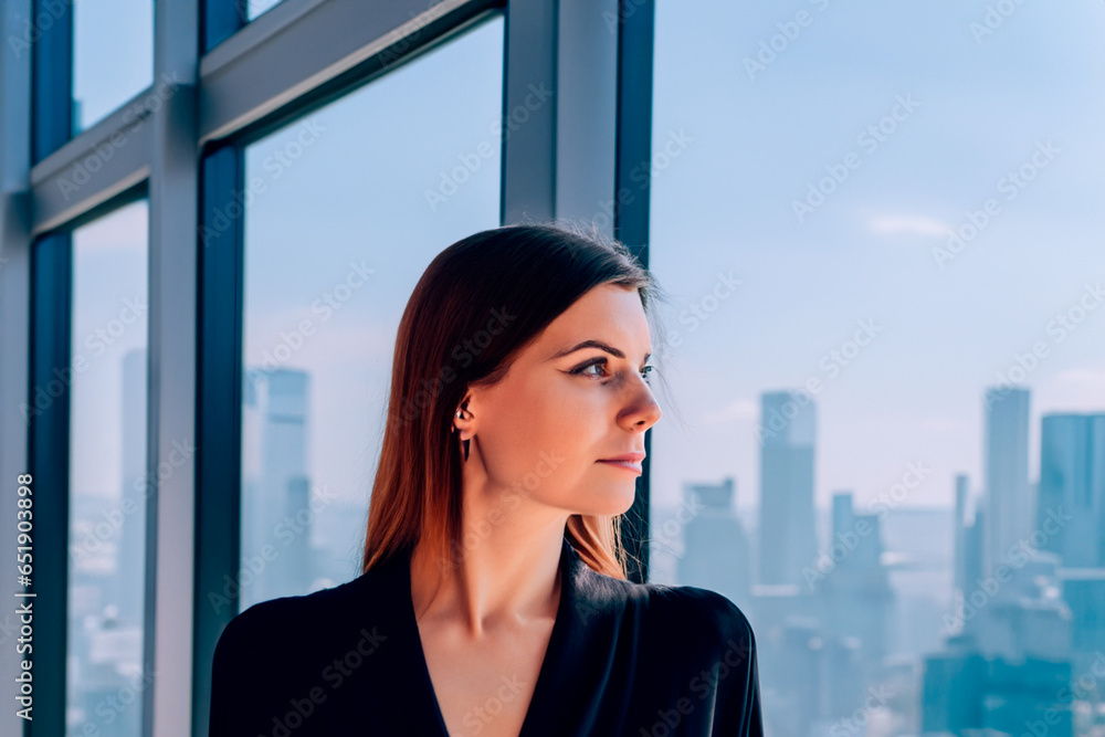 Fototapeta premium Pretty woman in office looks out window at skyscrapers