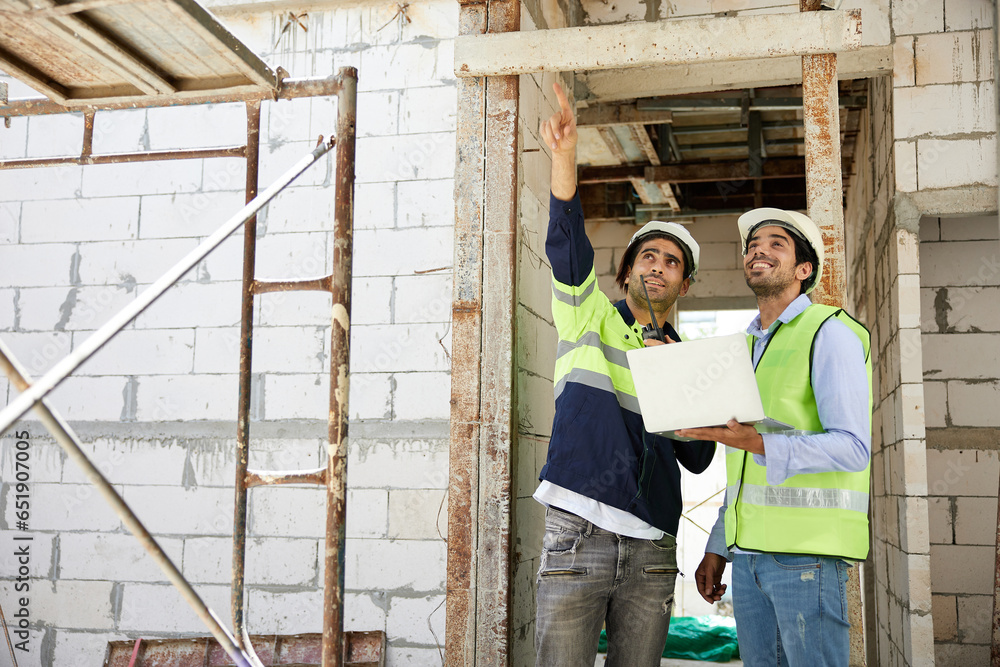 workers or architects working on laptop computer and pointing up to something at construction site