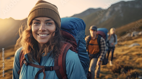 a Smiling young woman hiker with backpack looking at camera with group of friends hikers rises to the top of the hill. Hiker, Tourist camp. Generative Ai