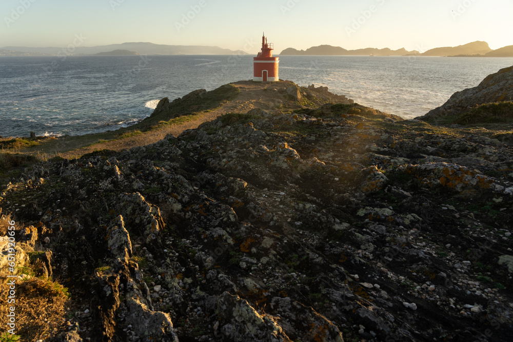 Punta Robaleira red lighthouse in Home cape at sunset in Rias Baixas zone in Galicia coast with Cíes islands in the background.