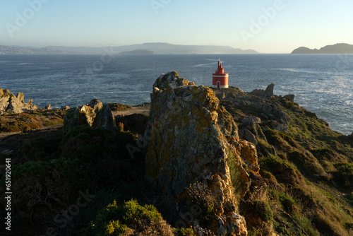 Punta Robaleira red lighthouse in Home cape at sunset in Rias Baixas zone in Galicia coast with Cíes islands in the background. photo