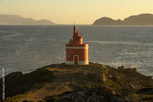 Punta Robaleira red lighthouse in Home cape at sunset in Rias Baixas zone in Galicia coast with Cíes islands in the background. photo