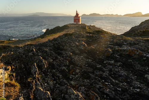 Punta Robaleira red lighthouse in Home cape at sunset in Rias Baixas zone in Galicia coast with Cíes islands in the background. photo
