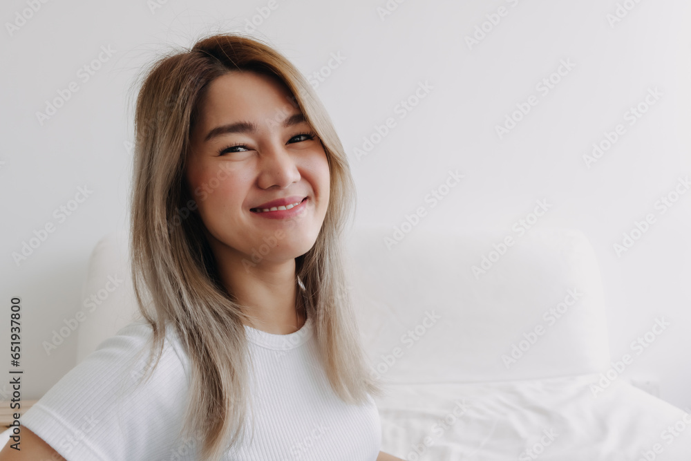 Asian woman smiling and looking at camera , wearing white top and sitting sofa at home alone with happy life. Asian woman smiling and looking at camera , wearing white top and sitting sofa at home alone with happy life.