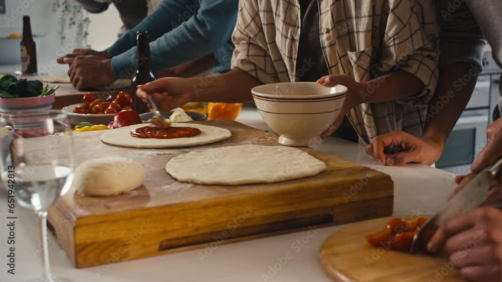 Group of friends at home in kitchen adding sauce to homemade pizzas for party together - shot in slow motion Group of friends at home in kitchen adding sauce to homemade pizzas for party together - shot in slow motion