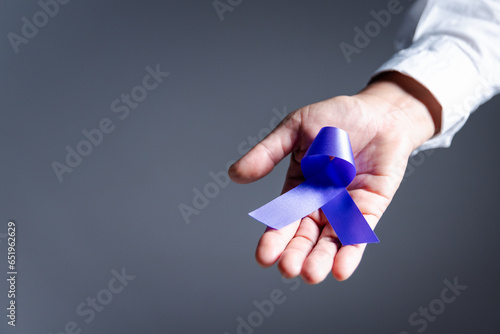 Woman with purple ribbon on grey background, closeup with space for text. Domestic violence awareness. Purple Ribbon for supporting people living. Healthcare and World cancer day concept.