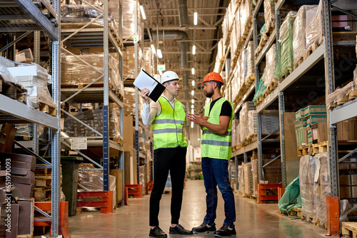 young managers in work wear organizing distribution in warehouse storage area. Caucasian men in green uniform discuss product delivery, having talk. in Warehouse full of Shelves with Goods