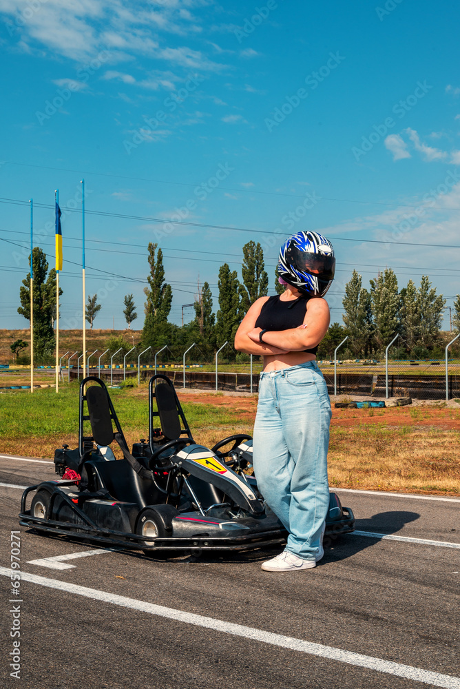 girl racer posing near a racing kart on the track in a helmet girl racer posing near a racing kart on the track in a helmet