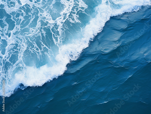 aerial perspective, the deep navy blue expanse of the ocean stretches out beneath, with white waves crashing and splashing against its surface.
