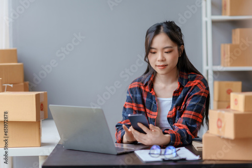 Beautiful Asian online business owner is using mobile phone checking with customer to check delivery address and phone number for accurate delivery. © amnaj
