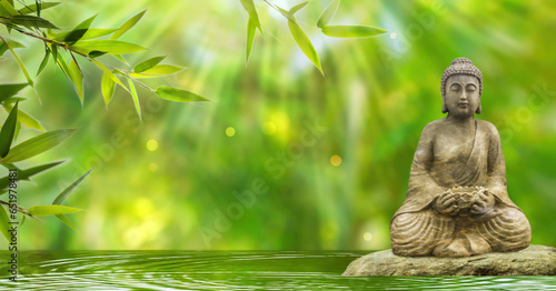 Fototapeta Naklejka Na Ścianę i Meble -  buddha statue in sunshine on a rock in a water wave on blurred abstract bamboo background, beautiful nature scene concept for travel, wellness spa or relaxation with asian spirit
