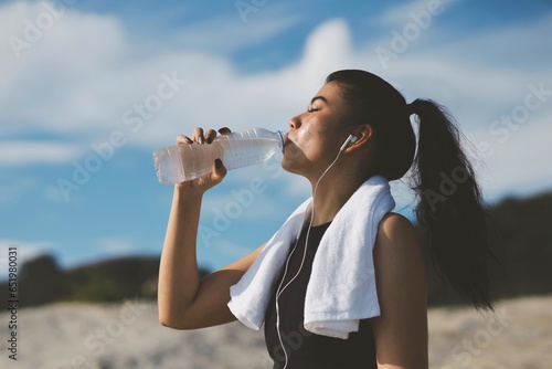 Beautiful woman drinking water after workout on the beach. photo