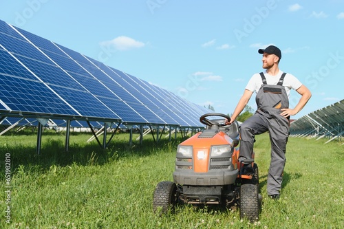 A man working at solar power station. A worker on a garden tractor mows grass on a solar panel farm.