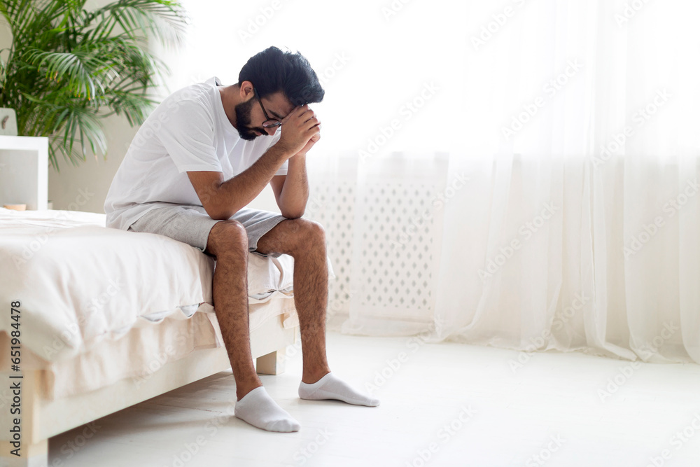 Portrait Of Depressed Young Indian Man Sitting On Bed At Home Portrait Of Depressed Young Indian Man Sitting On Bed At Home