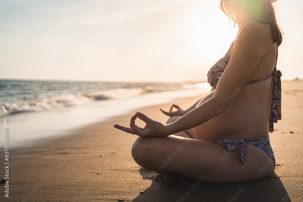 pregnant woman meditating sitting on the beach shore looking out to sea - obrazy, fototapety, plakaty 