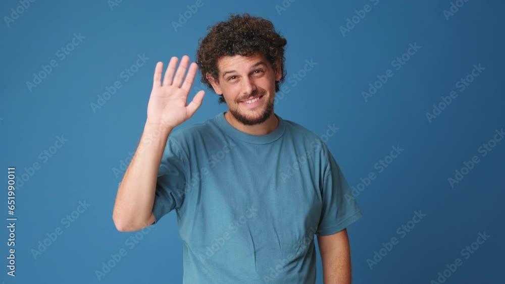 Happy man waving palm in greeting gesture isolated on blue background in studio Happy man waving palm in greeting gesture isolated on blue background in studio