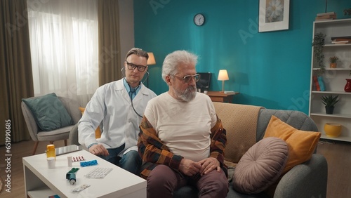 Full-size shot of a doctor checking up the condition of his patient at home. He is using stethoscope to examine breathing and heartbeat from the back.