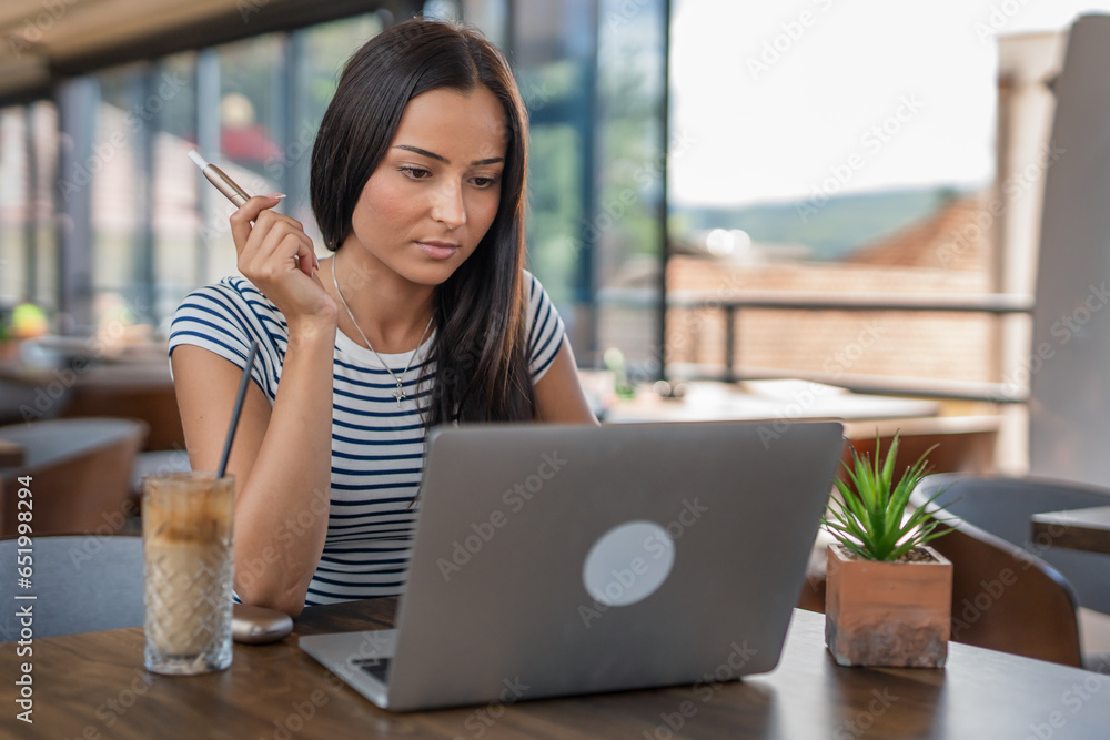 One woman sitting in cafe and holding electronic cigarette and working on laptop, modern lifestyle concept One woman sitting in cafe and holding electronic cigarette and working on laptop, modern lifestyle concept