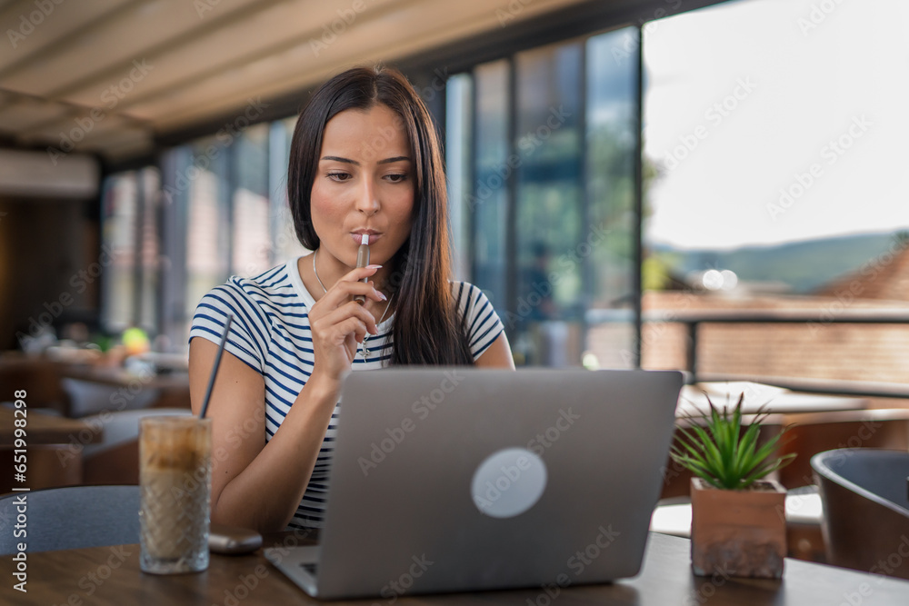 One woman sitting in cafe and holding electronic cigarette and working on laptop, modern lifestyle concept One woman sitting in cafe and holding electronic cigarette and working on laptop, modern lifestyle concept