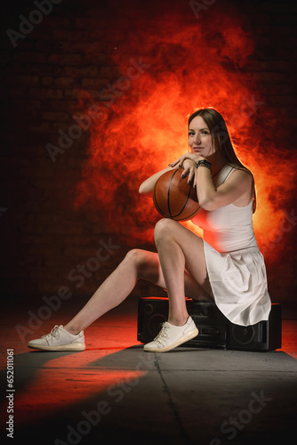 Young girl with the basketball ball posing on the red color smoke background.