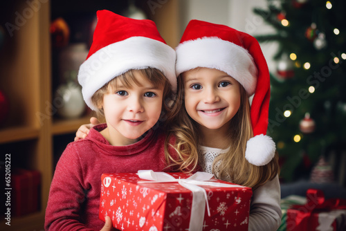 A boy and a girl are holding a Christmas present in their hands against the background of a Christmas tree. Family celebration
