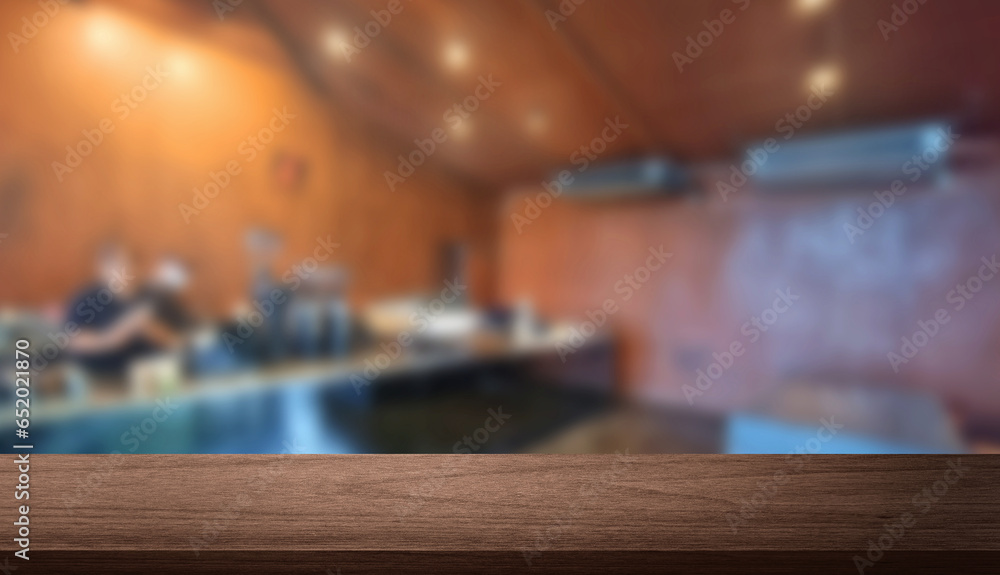 wooden table in foreground with spacious blurred interior of industrial cafe with rust walls, concrete floor, stainless steel counter and staff at background. indoor modern cafe, defocused view.