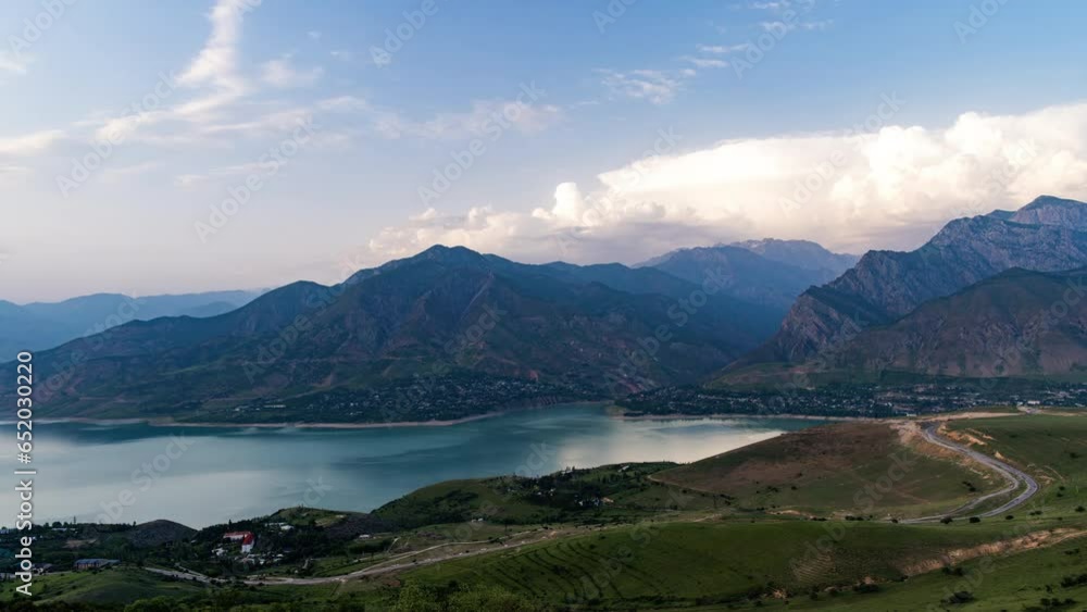 Mountains and lake video timelapse for background. Light percy clouds quickly fly in blue sky over mountains and lake or Charvak reservoir. Day turns into night. Village lights on shore of lake Mountains and lake video timelapse for background. Light percy clouds quickly fly in blue sky over mountains and lake or Charvak reservoir. Day turns into night. Village lights on shore of lake