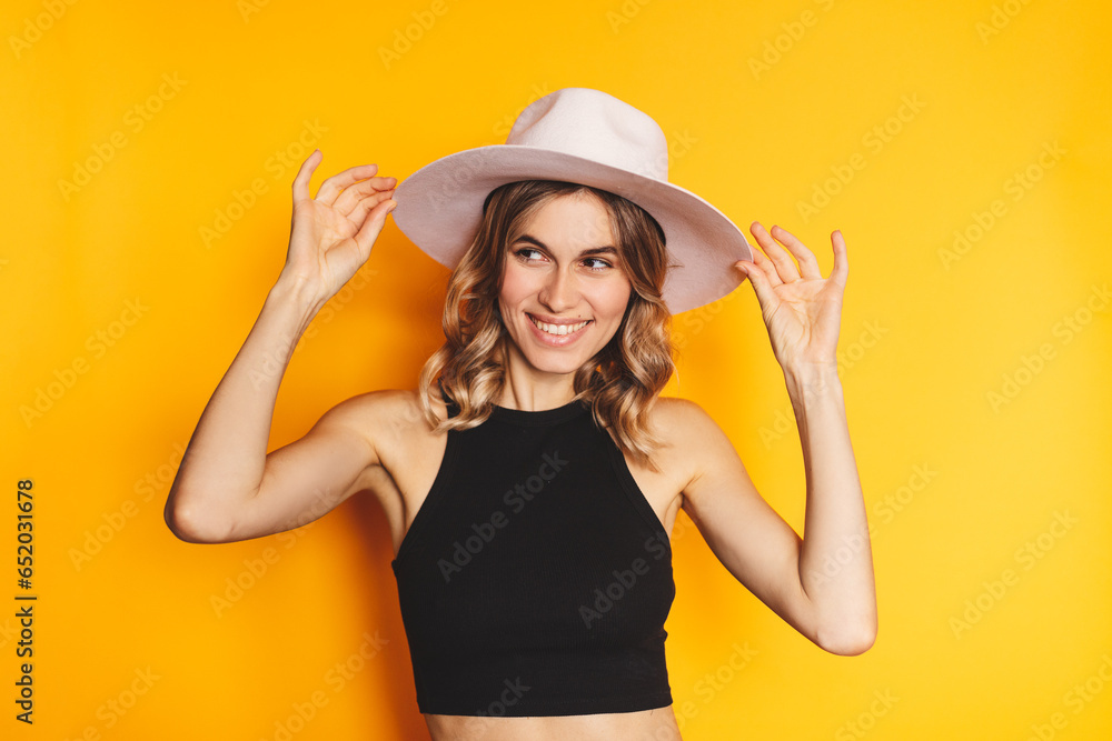 Curly blonde hair woman touch her white hat and look at side isolated on yellow background. Summertime or vacation concept. Curly blonde hair woman touch her white hat and look at side isolated on yellow background. Summertime or vacation concept.