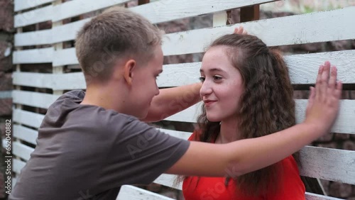 First love teenage boy pesters girl, talks and hugs. Teenage girl is smiles.