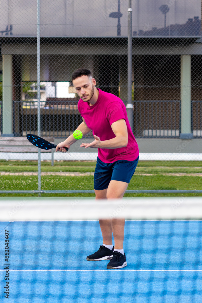 Portrait of a man performing a serve in pickleball. Sporty man pickleball tennis player trains on the outdoor court using a racket to hit ball